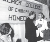 HT Hughes (rt) presenting college president, Dave Palmer (lft), a gold Chiropractic Diamond Jubilee Commemorative Medal at the 1969 Palmer Homecoming. (Agnes Palmer - extreme left)